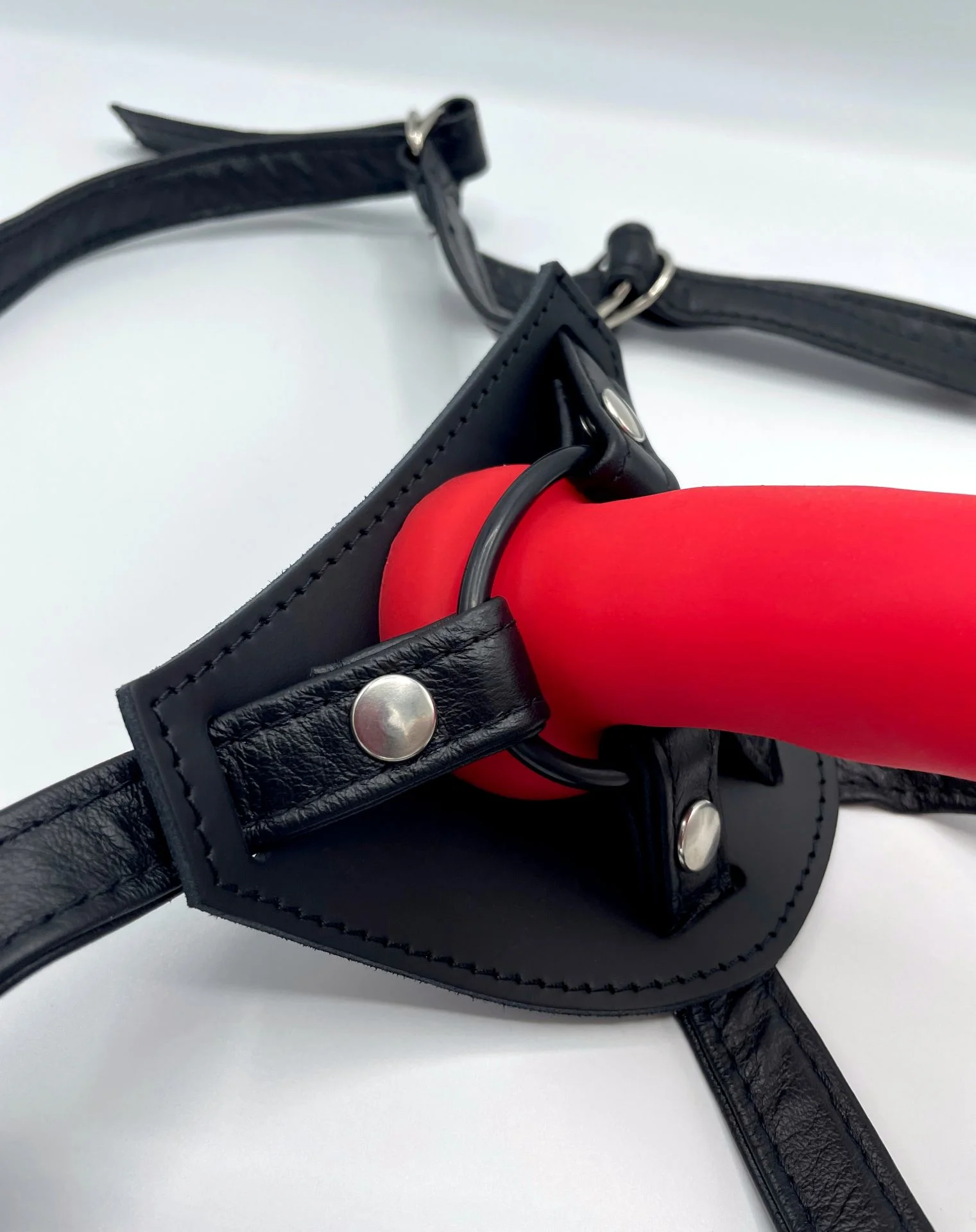 Nahaufnahme der O-Ring-Halterung am Leder-Strap-on-Harness mit Lederschlaufen und Druckknöpfen, mit rotem Dildo